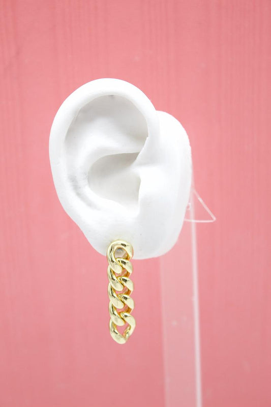 A white mannequin ear displays a stylish gold chain link dangle earring against a pink background.
