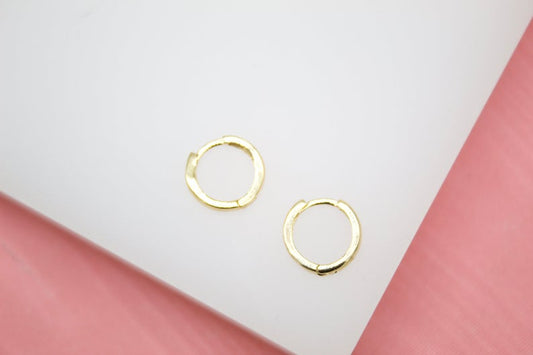 A pair of small gold hoop earrings rests on a white display surface.