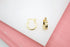 A pair of polished gold hoop earrings rests on a white display surface against a pink background.