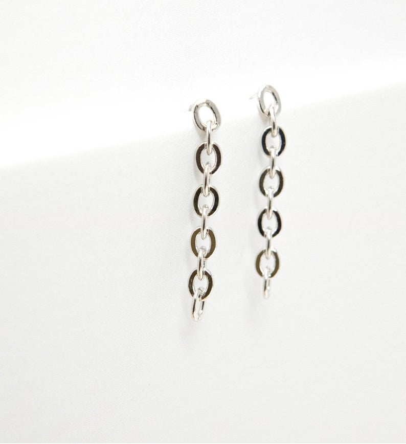 A pair of minimalist silver chain link drop earrings rests against a clean white background.