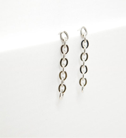 A pair of minimalist silver chain link drop earrings rests against a clean white background.