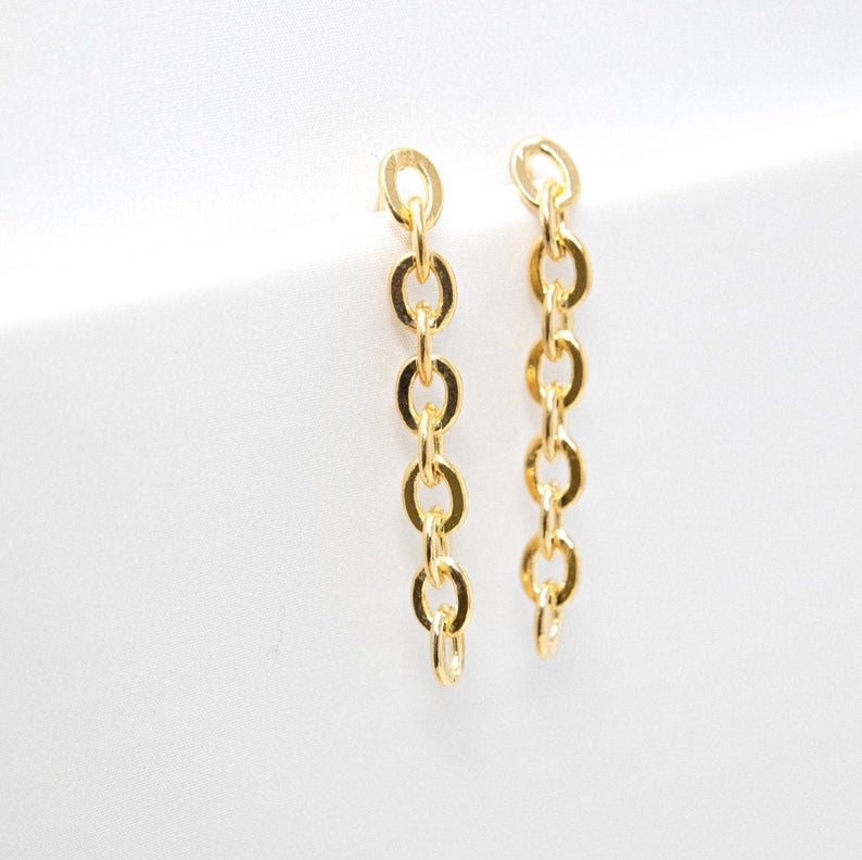 A pair of dangling gold chain-link earrings rests against a clean white background.