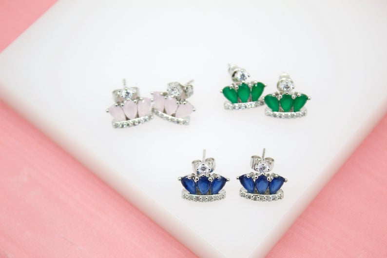 Three pairs of sterling silver crown-shaped stud earrings featuring colorful gemstone teardrops and cubic zirconia accents rest on a white display surface.