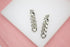 A pair of shiny silver chain link earrings rests neatly on a white display surface against a soft pink background.