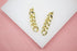 A pair of polished gold cuban link drop earrings rests on a white display surface.