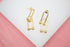A pair of elegant gold paperclip link earrings with small ball details rests on a white display surface.