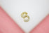 A pair of gold huggie hoop earrings encrusted with sparkling cubic zirconia stones rests on a white display surface against a soft pink background.
