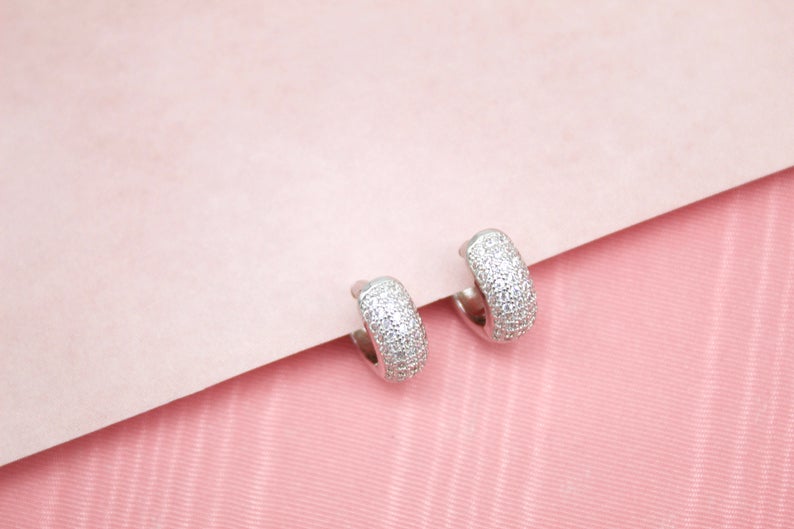 A pair of sparkling pavé-set silver hoop earrings rests on a soft pink background.