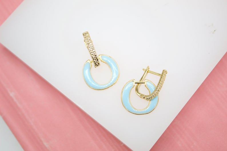A pair of elegant gold hoop earrings featuring light blue enamel accents rests on a white display surface.