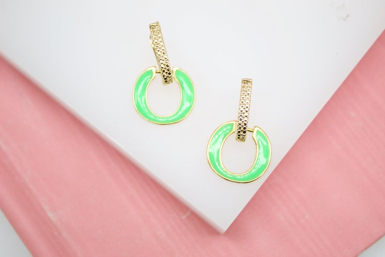 A pair of gold earrings featuring textured rectangular posts and bright neon green enamel hoops rests on a white display block.
