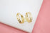 A pair of gold hoop earrings embellished with sparkling cubic zirconia stones sits upright against a white and pink background.