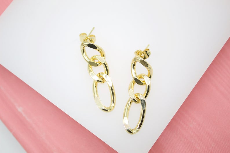 A pair of polished gold chain link drop earrings rests on a white and pink surface.