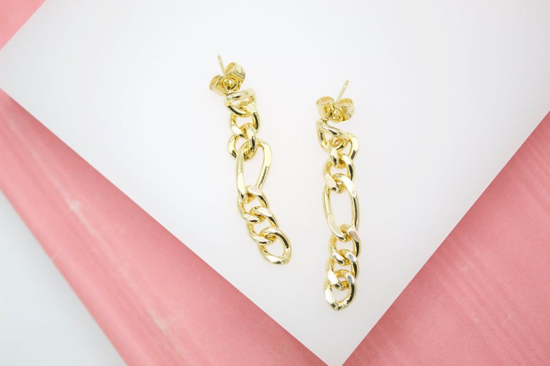 A pair of shiny gold chain link drop earrings rests on a pink and white surface.