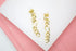 A pair of shiny gold chain link drop earrings rests on a pink and white surface.