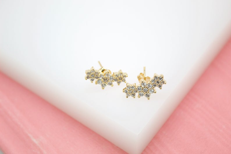 A pair of gold flower cluster earrings sparkle on a white and pink display surface.