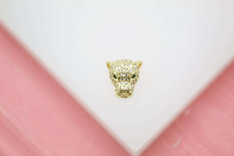 A gold panther pendant encrusted with sparkling clear cubic zirconia stones and featuring vibrant green gemstone eyes rests on a white surface.