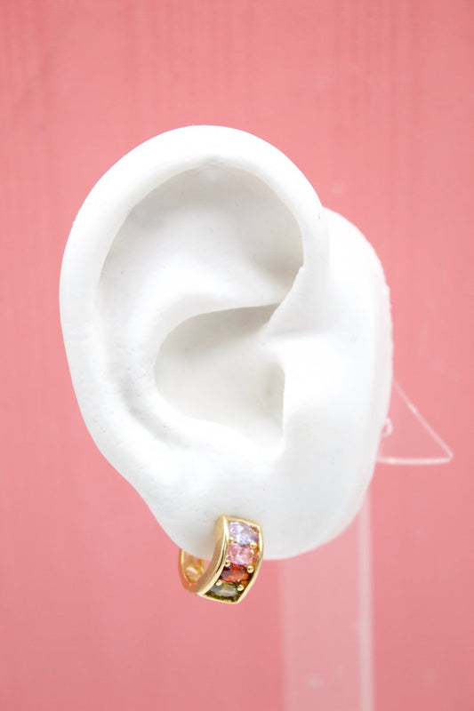 A white display mannequin ear showcases a small gold huggie hoop earring encrusted with multicolored cubic zirconia stones.