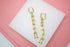 A pair of gold chain-link dangle earrings featuring geometric links and small bead details rests on a white display surface against a pink background.
