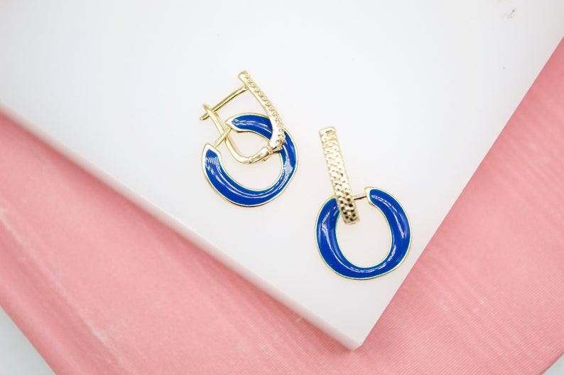 A pair of elegant gold hoop earrings featuring vibrant blue enamel and textured posts rests on a clean white display surface.