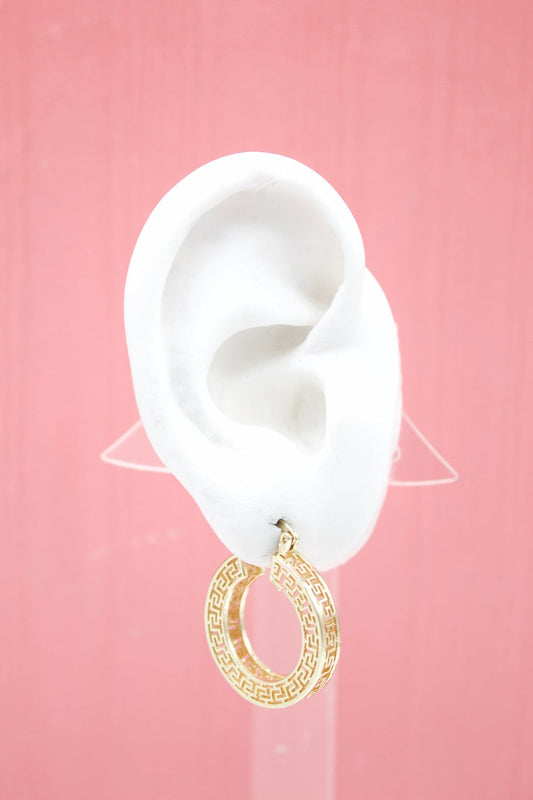 A white mannequin ear displays a gold Greek key hoop earring against a pink background.