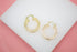A pair of gold Greek key hoop earrings rests on a white display stand.