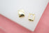 A pair of small, shiny gold hoop earrings rests on a white and pink display surface.