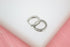A pair of silver huggie hoop earrings featuring sparkling pave crystals rests on a white display surface.