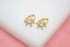 A pair of gold huggie hoop earrings featuring sparkling cubic zirconia stones arranged in a floral pattern rests on a white display surface.