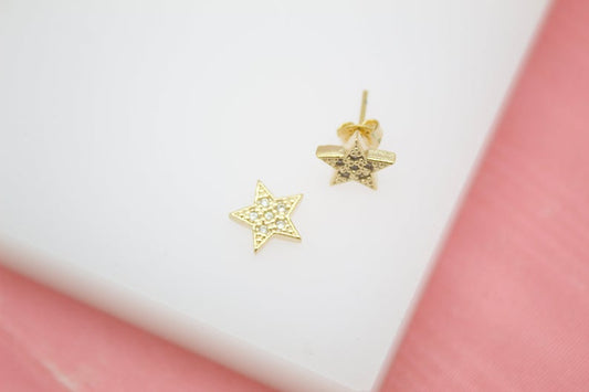 A pair of sparkling gold star stud earrings rests on a white surface.