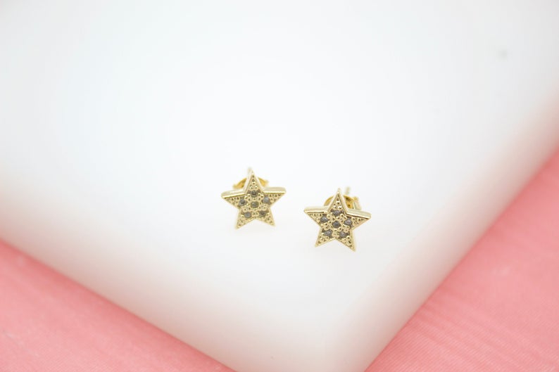 A pair of gold star stud earrings encrusted with small clear crystals rests on a white surface.