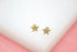 A pair of gold star stud earrings encrusted with small clear crystals rests on a white surface.
