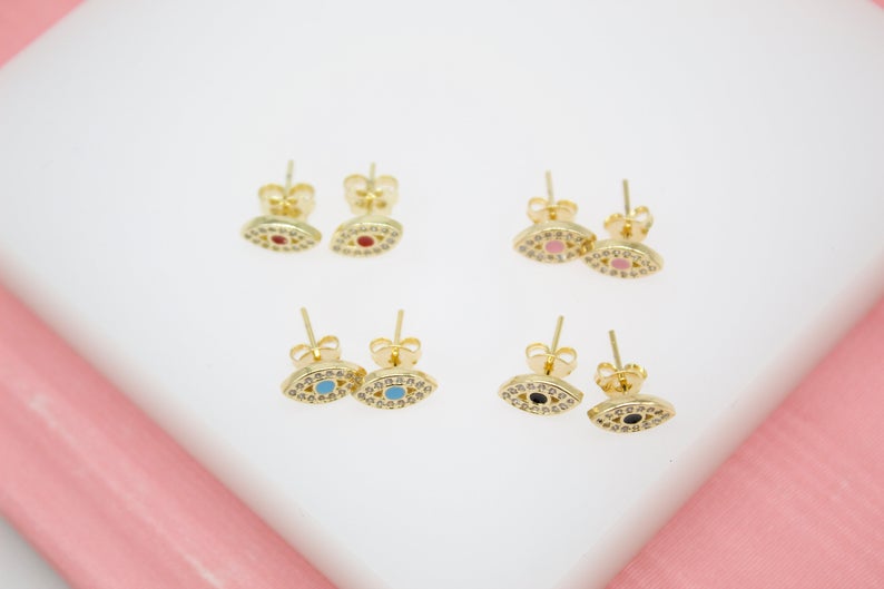 Four pairs of gold evil eye stud earrings with colorful enamel centers display on a white surface.