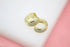 A pair of gold huggie hoop earrings featuring sparkling pavé crystals rests on a white surface.