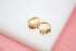 A pair of gold huggie hoop earrings features colorful multi-gemstone baguettes resting on a white display surface.