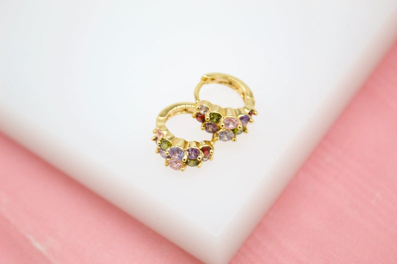 A pair of gold hoop earrings embellished with colorful cubic zirconia stones rests on a white surface.