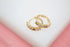 A pair of gold hoop earrings features vibrant multicolored gemstones set along the bands against a soft white and pink background.