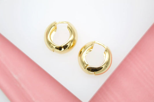 A pair of polished gold hoop earrings rests on a light background.