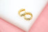 A pair of gold huggie hoop earrings embedded with sparkling cubic zirconia stones rests on a white display block.