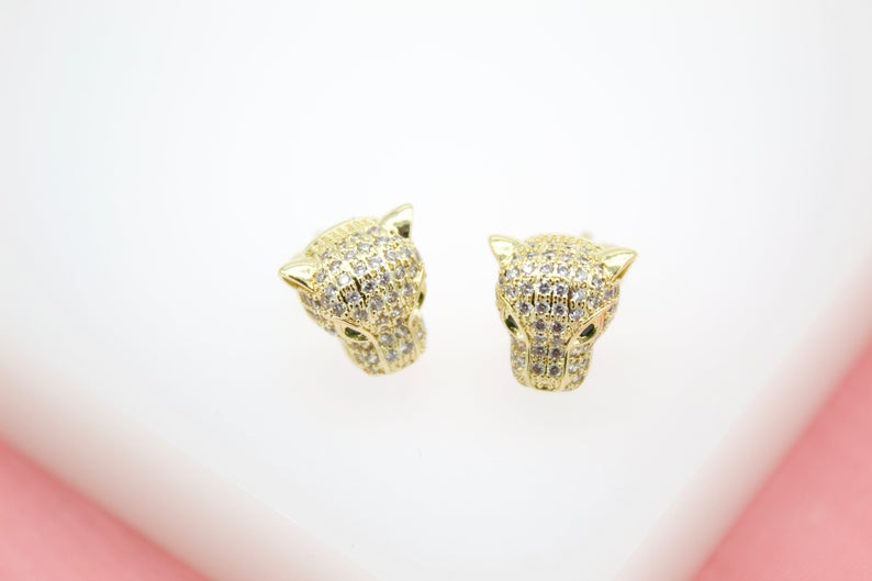 A pair of gold panther head stud earrings encrusted with sparkling cubic zirconia stones rest on a white display surface.