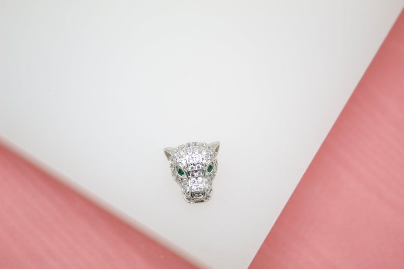 A sparkling diamond and emerald panther head pendant rests on a clean white display surface.