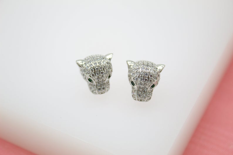 A pair of sparkling silver panther-shaped stud earrings sparkle with pave-set cubic zirconia stones and vivid green crystal eyes against a clean white surface.
