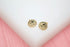 A pair of polished gold sun face stud earrings rests on a white and pink display stand.