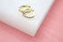 Two delicate gold hoop earrings studded with sparkling cubic zirconia rest on a white display block.