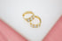 A pair of gold huggie hoop earrings embedded with sparkling cubic zirconia stones rests on a white and pink surface.