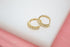 A pair of shimmering gold hoop earrings set with sparkling cubic zirconia stones rests against a soft white and pink background.