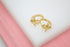 A pair of gold huggie hoop earrings featuring sparkling crystal-emborted bows rest on a white display surface.