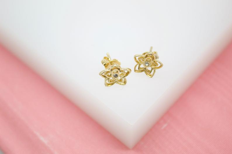 A pair of gold flower stud earrings with sparkling crystal centers rests on a white display surface.