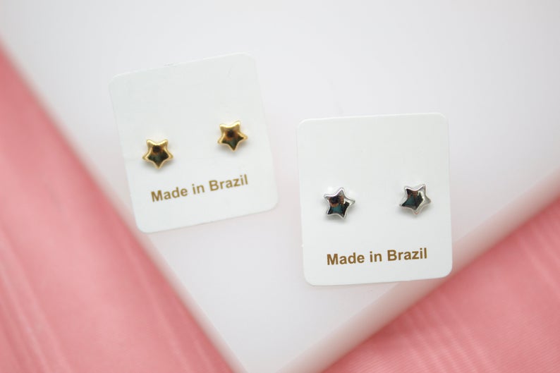 Two pairs of star-shaped stud earrings, one in gold and one in silver, are displayed on white cards marked "Made in Brazil".