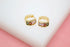 A pair of gold huggie hoop earrings featuring sparkling multicolored gemstones sits on a white surface against a pink background.