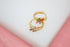 A pair of gold huggie hoop earrings decorated with colorful baguette cubic zirconia stones rests on a white display surface against a soft pink background.